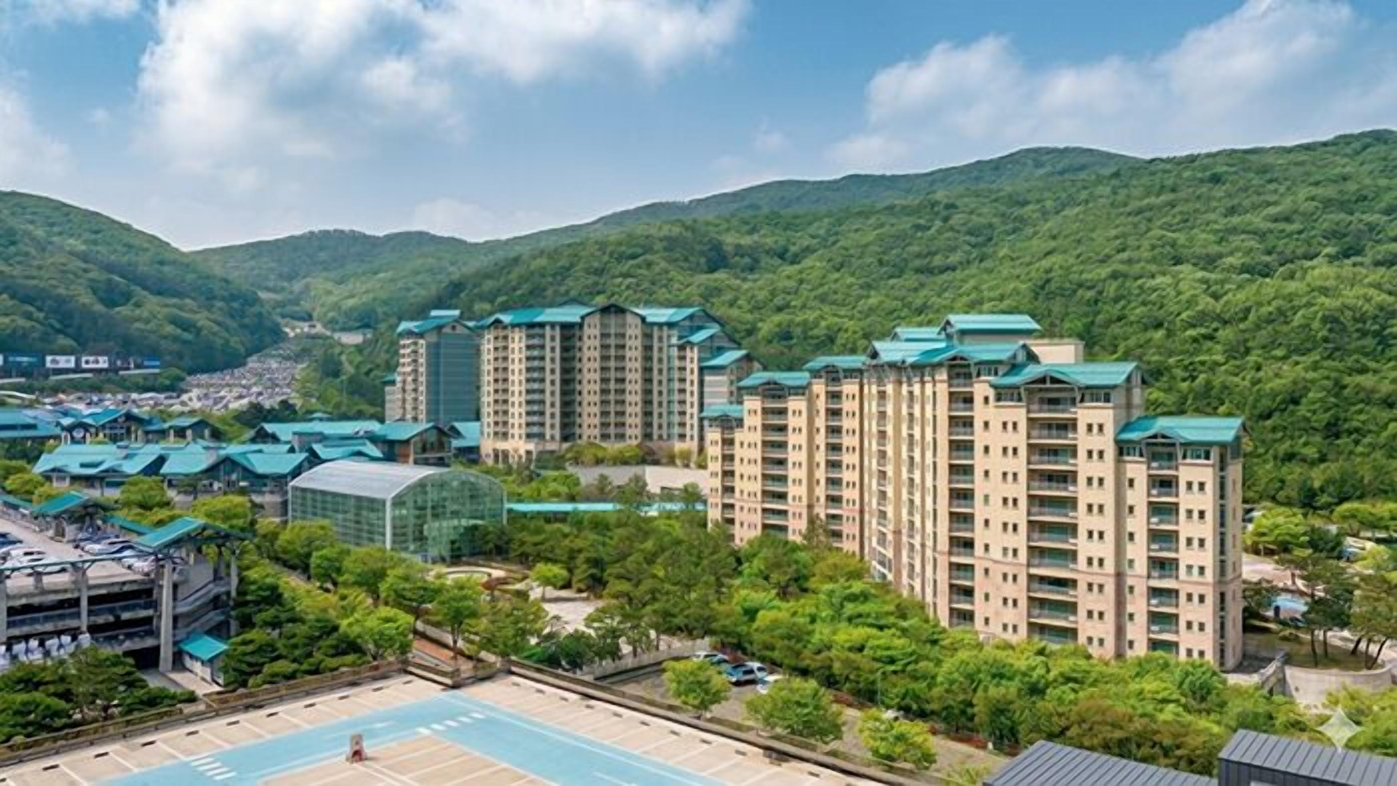 A multi-story hotel with a green roof, surrounded by lush greenery and hills.