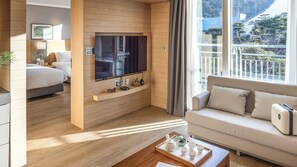 Habitación de hotel con cama, sofá, televisor montado en una pared de madera y balcón con vistas.