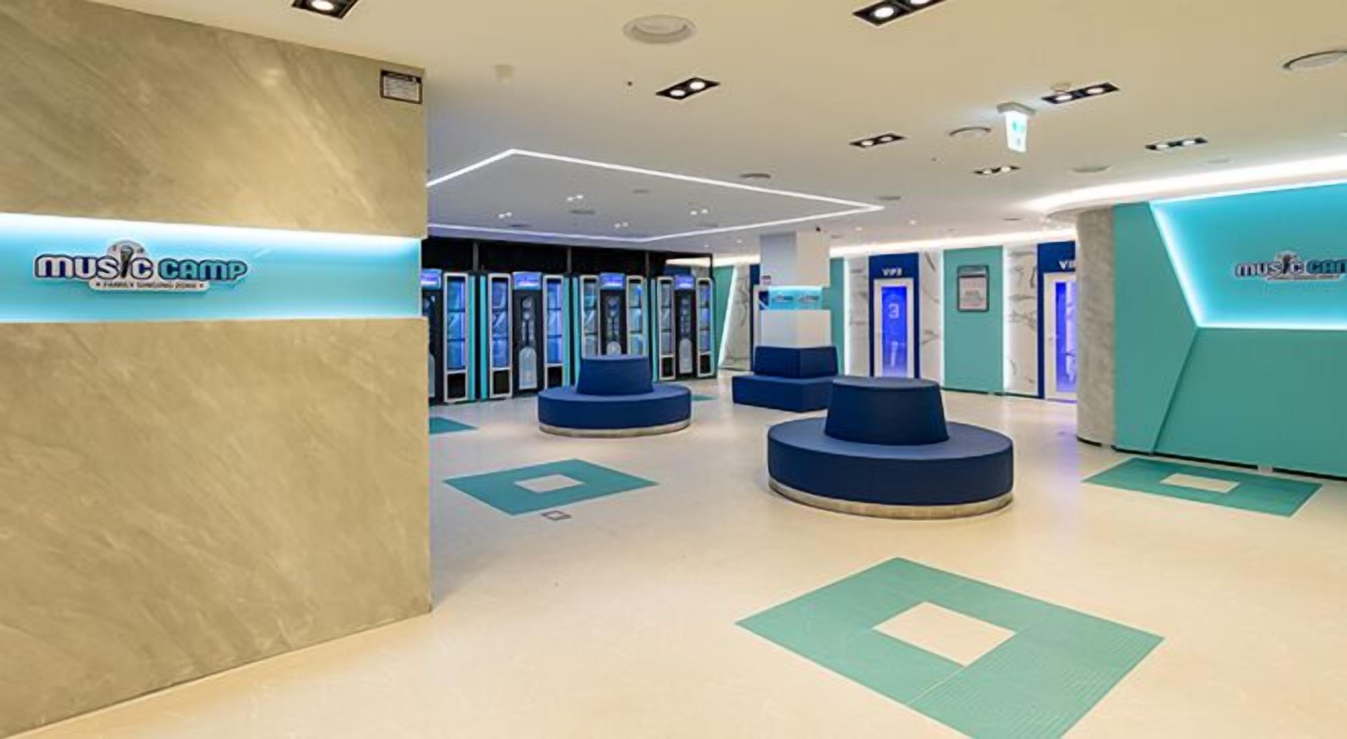 A modern lobby with a 'Music Camp' sign, seating areas, and a reception desk.
