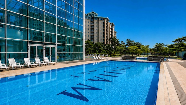 A swimming pool with lounge chairs and a modern building in the background.