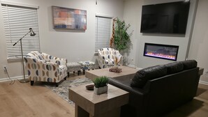 A living room with a sofa, armchairs, a coffee table, a TV, and a fireplace.