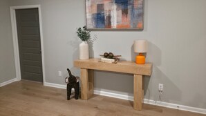 A room with a wooden console table, a potted plant, decorative items, and a painting on the wall.