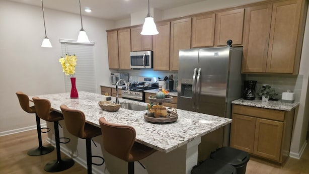 A modern kitchen with a central island, bar stools, stainless steel appliances, and pendant lighting.