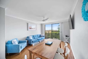 Ein modernes Wohnzimmer mit einem Holzespeisetisch, blauen Sofas und einem großen Fenster mit Blick ins Grüne.