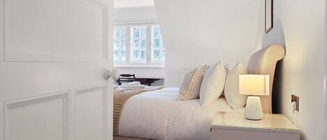 A bedroom with a bed, bedside table, lamp, and a window with a view.