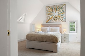 Ein Schlafzimmer mit einem Bett, einem Nachttisch, einem Fenster und einem an der Wand hängenden abstrakten Gemälde.