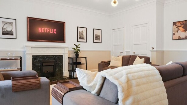 Ett vardagsrum med en öppen spis, en soffa, ett soffbord och en tv-apparat som visar ”NETFLIX”.