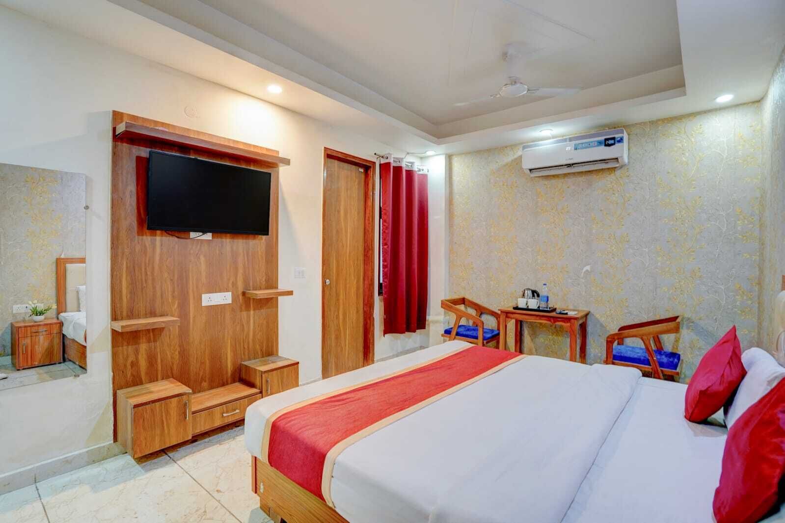 A hotel room with a bed, a TV, a wardrobe, a desk, and an air conditioning unit.