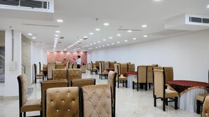 A spacious dining area with multiple tables and chairs, air conditioning units, and a marble floor. - Hotel Gray Stone (Noida)