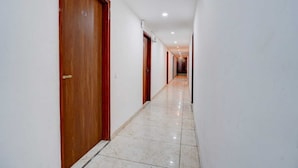 A corridor with wooden doors, white walls, and a tiled floor. - Hotel Gray Stone (Noida)