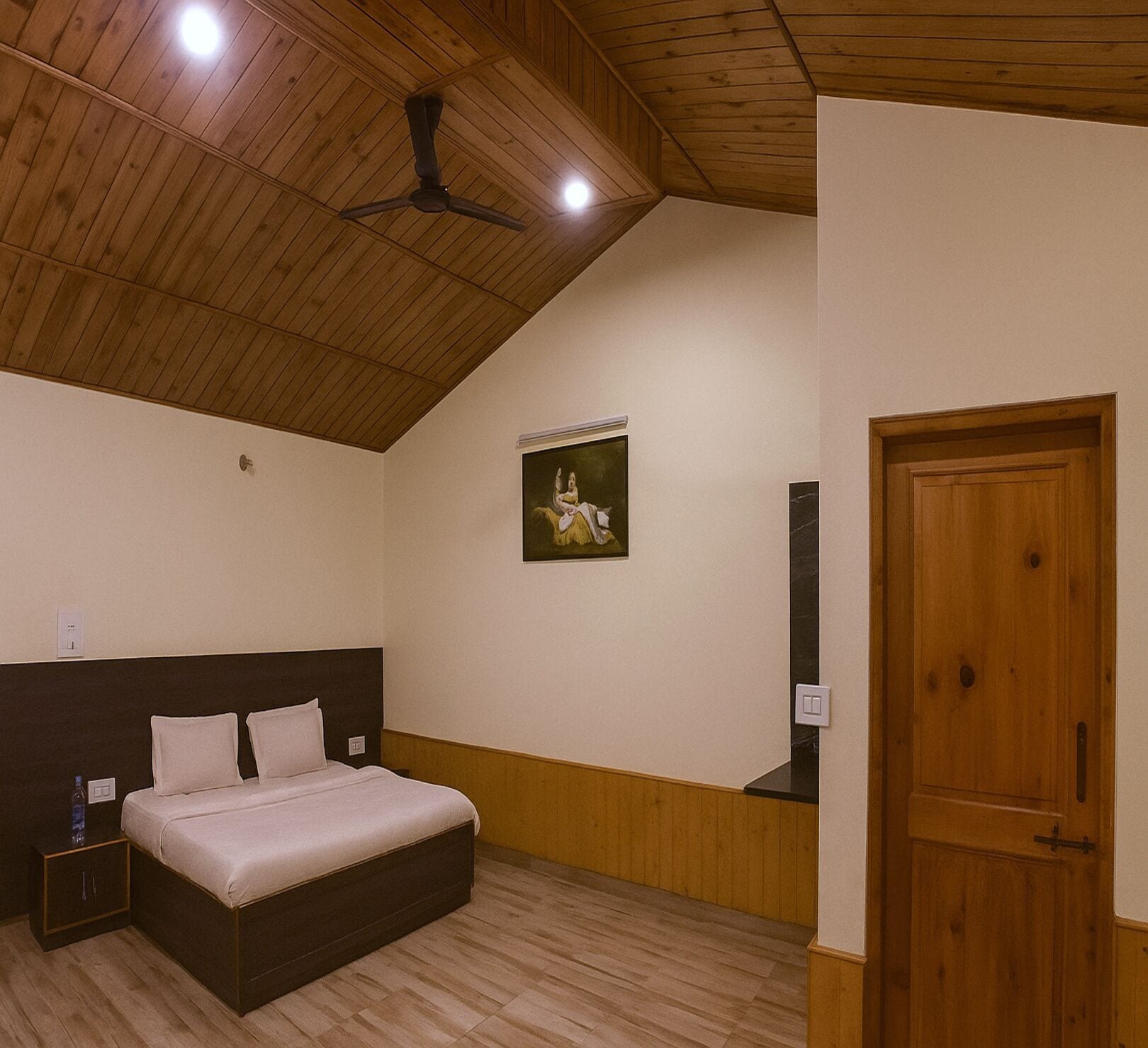 A bedroom with a wooden ceiling, a bed with a headboard, a nightstand, a wall-mounted painting, and a door.
