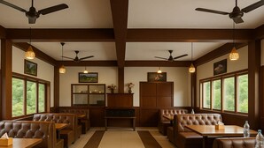 A restaurant with booths and tables, ceiling fans, and large windows. - Chaman Vatika (Kasol)