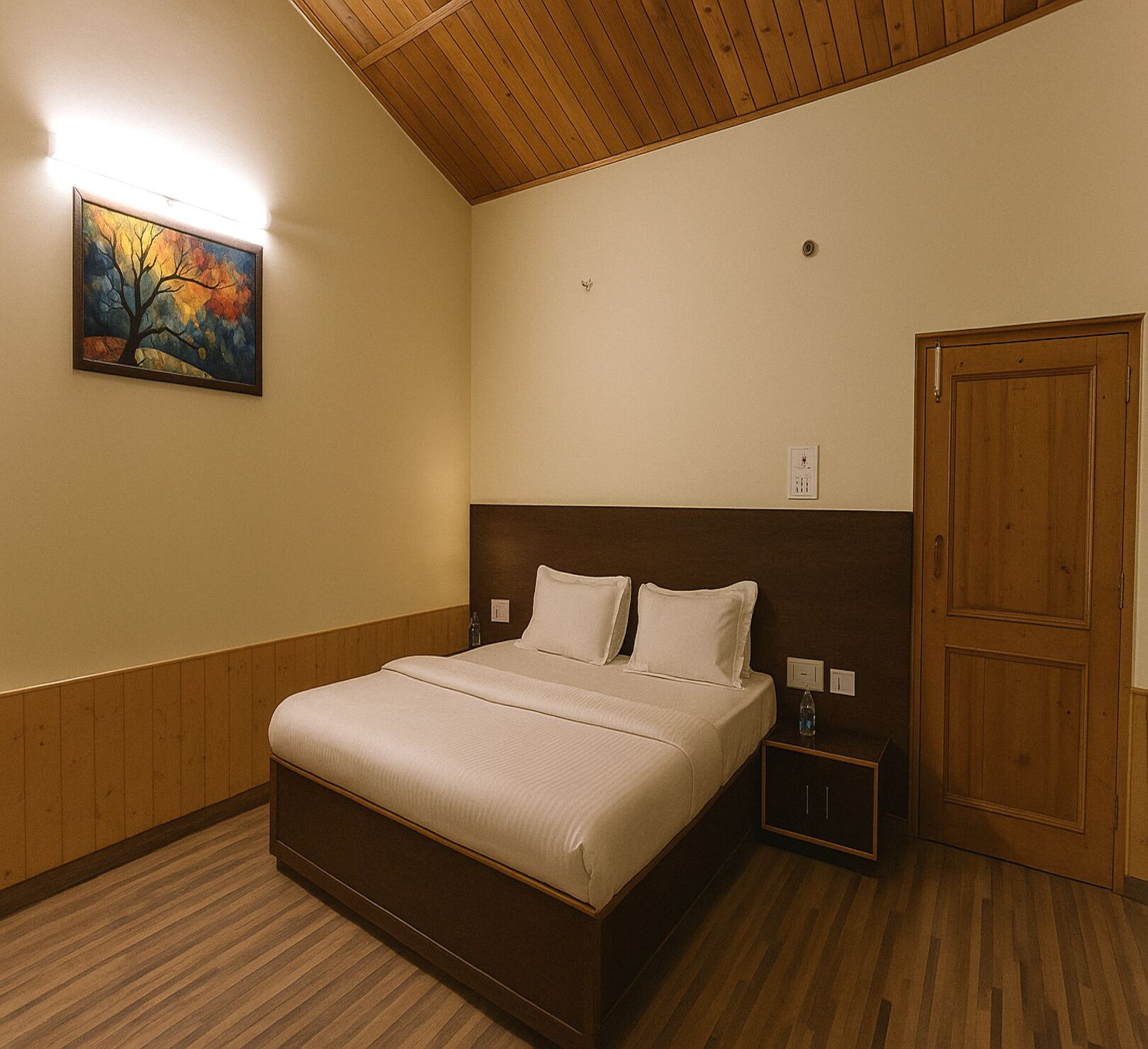 A hotel room with a wooden headboard, a bed with white linens, a nightstand with a bottle, and a painting on the wall.