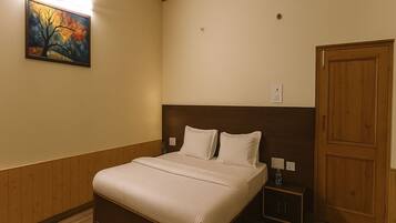 A hotel room with a wooden headboard, a bed with white linens, a nightstand with a bottle, and a painting on the wall.