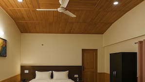 A hotel room with a wooden ceiling, a bed with white bedding, a nightstand, a wardrobe, and a door. - Chaman Vatika (Kasol)