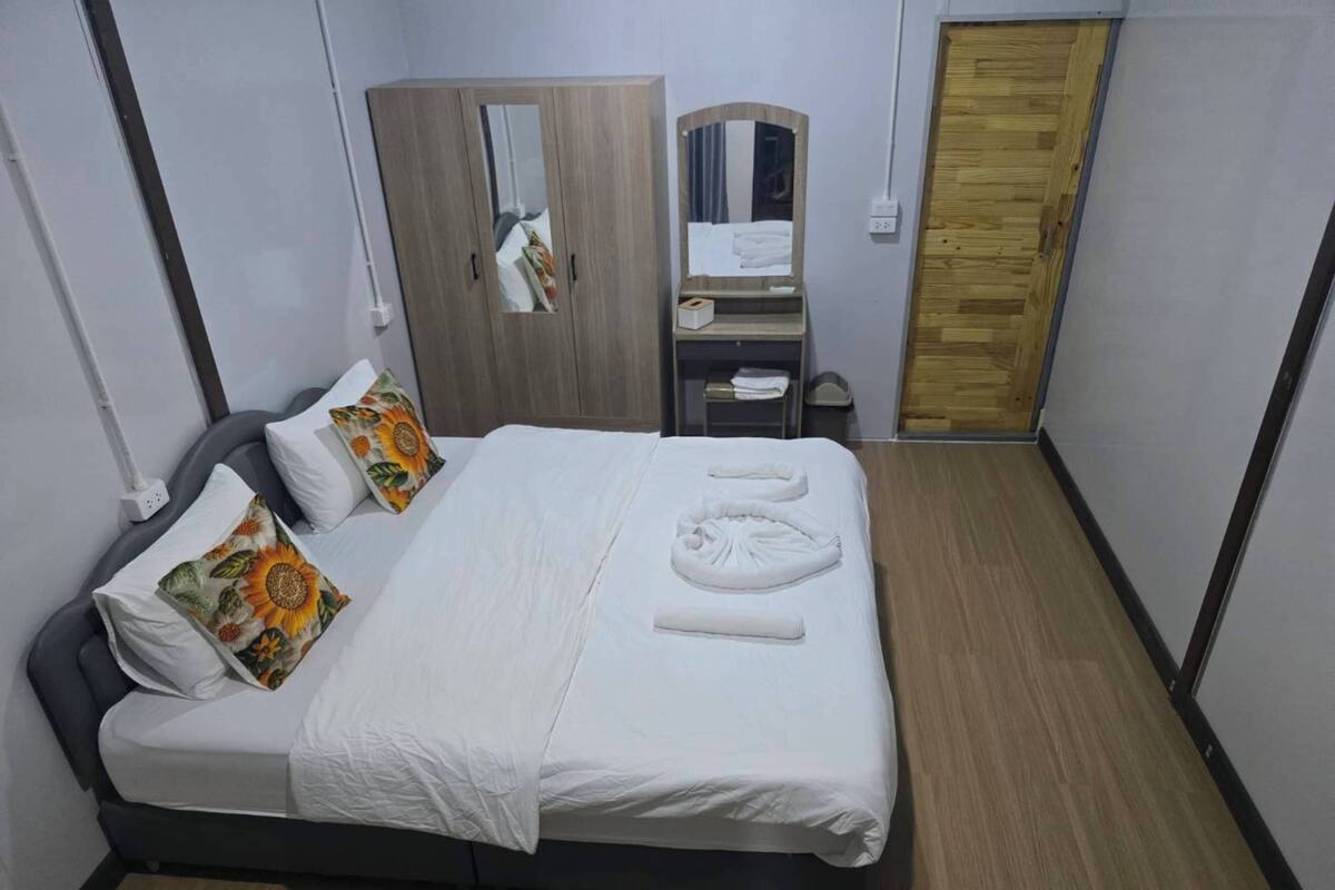A neatly made bed with white linens, a mirror above it, and a wooden wardrobe with a mirror.