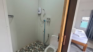 A small bathroom with a shower, toilet, and a bed visible through an open door. - Oasis Phamee (Ko Pha-ngan)