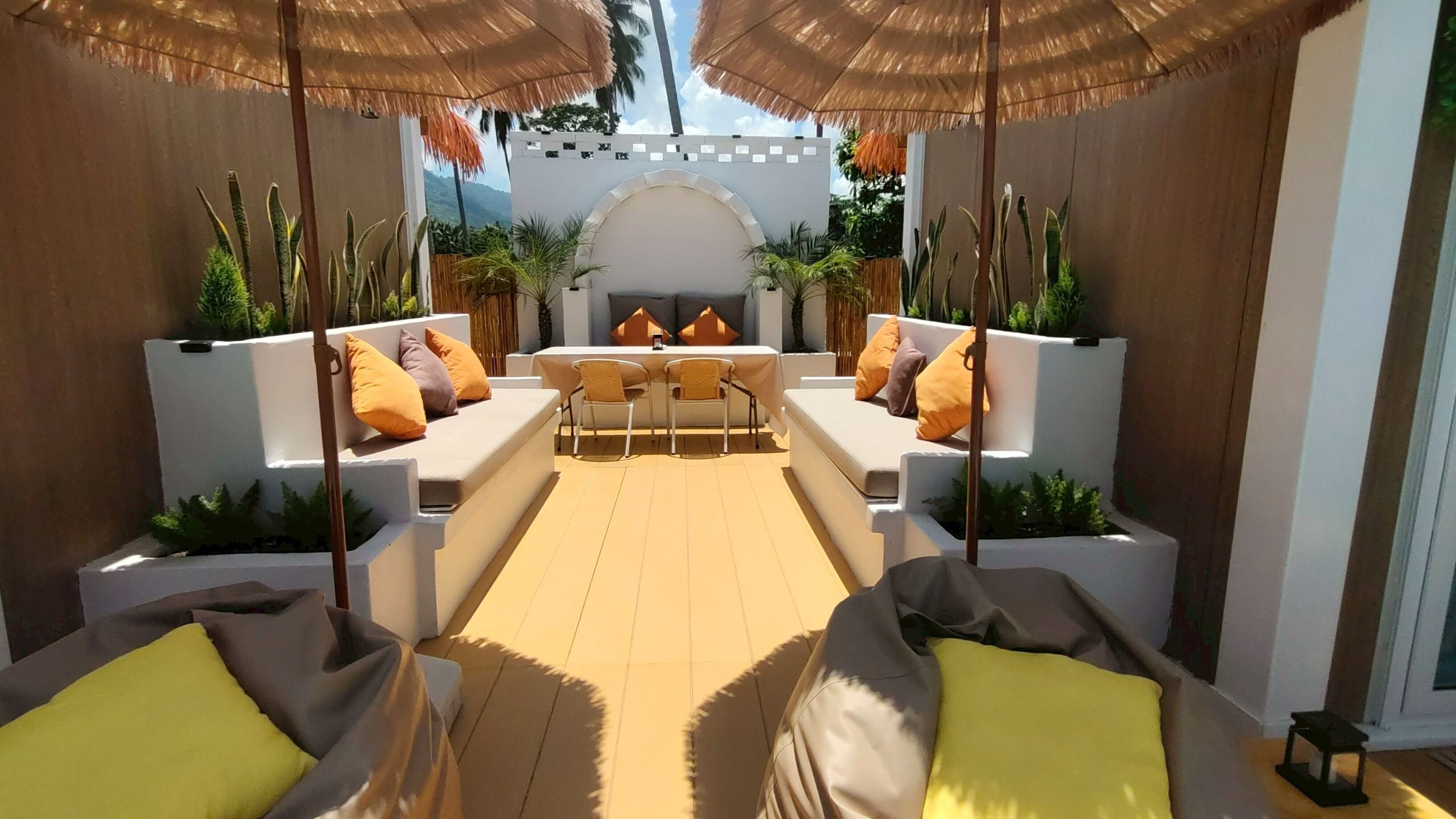Un espace extérieur lumineux, aménagé avec des canapés blancs, des coussins jaunes et une table centrale entourée de chaises.