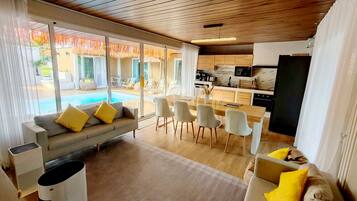 Un salon moderne comprenant un canapé, des chaises de salle à manger, un coin cuisine et une vue sur la piscine.