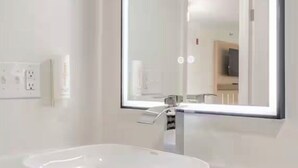 A modern bathroom with a white sink, a large mirror, and a visible electrical outlet on the wall.