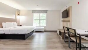 A hotel room with a bed, a desk, a chair, a TV mounted on the wall, and a window.