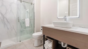 A modern bathroom with a glass shower enclosure, a white toilet, a large mirror, and a white sink.