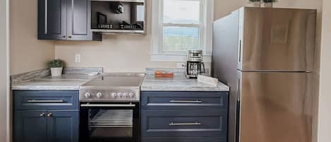Una cocina con armarios oscuros, estufa de acero inoxidable, horno, refrigerador y ventana con vistas.