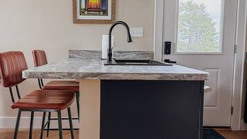 A kitchen with a marble countertop, a black sink, and a pendant light.