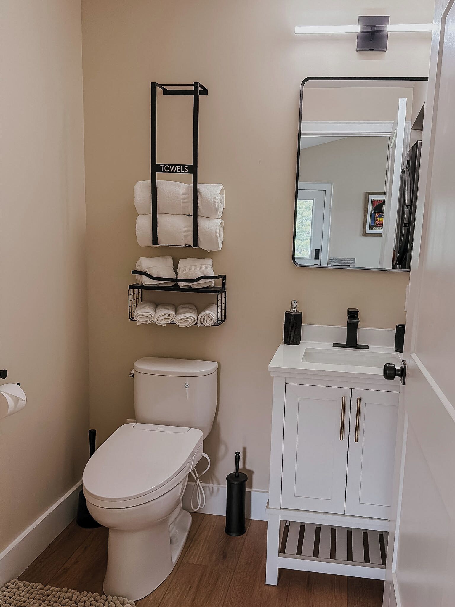 A bathroom with a toilet, a sink, a mirror, and towel storage.