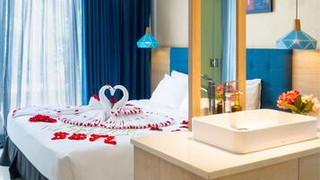 A hotel room with a bed, a white bedside table, a bathroom with a sink, and a mirror.