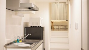 Una cucina compatta con piano cottura, lavello e forno a microonde. Una scala conduce a una camera da letto con un letto e una finestra con tende.