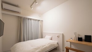 Una camera da letto con un letto, un comodino, un tavolo di fianco al letto, un condizionatore d'aria a parete e una finestra con tende.