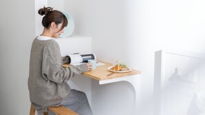 Una persona seduta a un tavolo di legno con un piatto di cibo, un bicchiere e un libro.