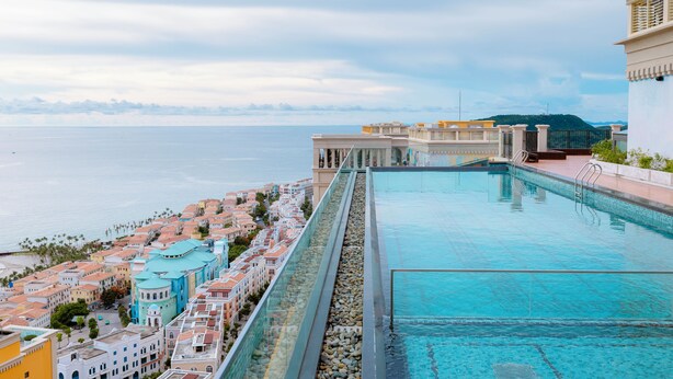 Una piscina en la azotea con vistas al mar y edificios coloridos.