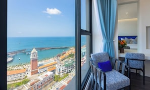 A room with a large window overlooking a coastal cityscape, including a clock tower and a bridge. - Hillside Gallery Phu Quoc Condotel (Phu Quoc)