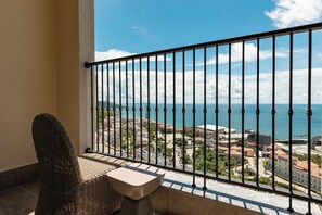 A balcony with a wicker chair and a small table, overlooking a coastal cityscape with buildings and the sea. - Hillside Gallery Phu Quoc Condotel (Phu Quoc)