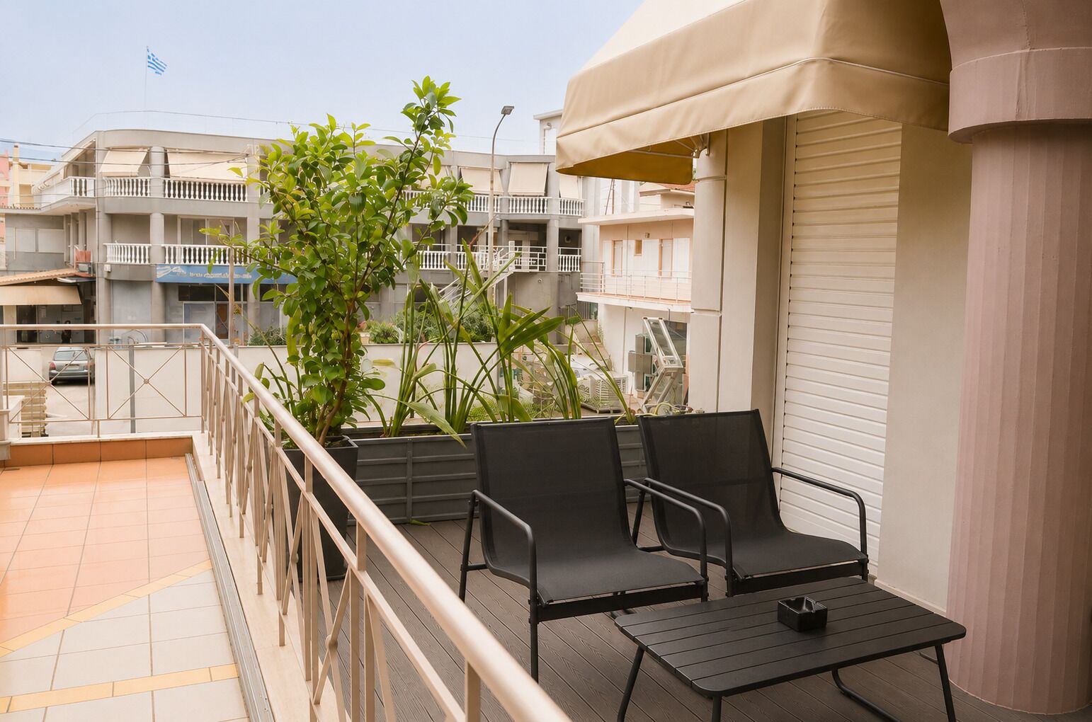 A balcony with two chairs and a table, potted plants, and a view of neighboring buildings.