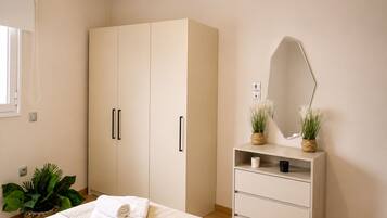 A bedroom with a bed, a wardrobe, a vanity with a mirror, and two potted plants.