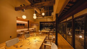 Un comedor con mesas y sillas de madera, una zona de bar y amplias ventanas que ofrecen vistas al exterior.