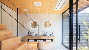 Un baño moderno con una escalera de madera, un espejo redondo, un lavamanos y un ventanal amplio.