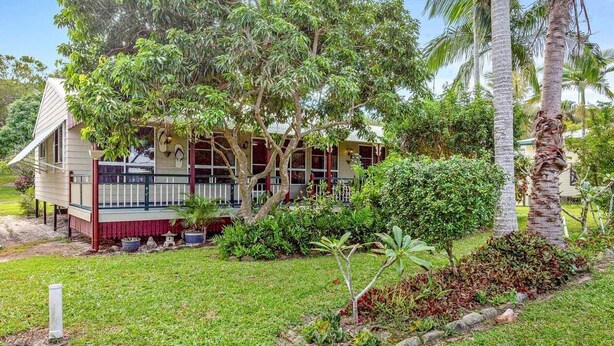 Une maison dotée d’un porche, entourée d’une végétation luxuriante et de palmiers.