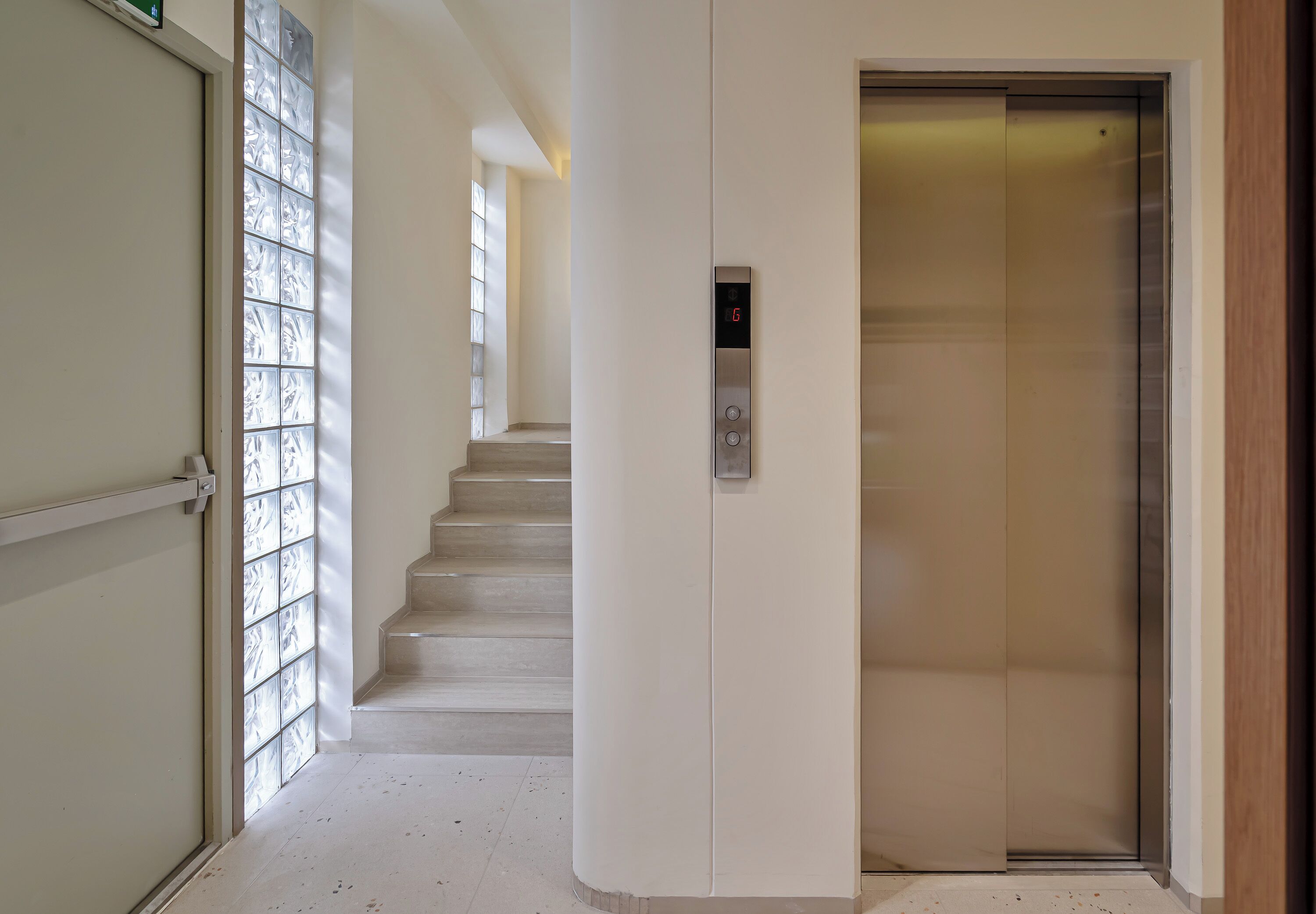 A hallway with a glass door, a staircase, and an elevator.