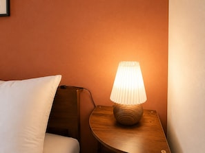 A bedside table with a lamp, a pillow, and a wooden nightstand against a wall.