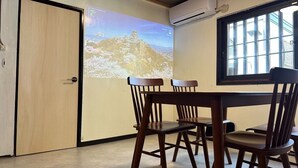 A room with a wooden table and chairs, a projection screen displaying a landscape, and an air conditioning unit on the wall. - Quiet inn in Takatsuki/6 min. from station/13 min. from Kyoto, 15 min. from Osaka/ 1 hr. from Kansai Airport by direct train/ Japanese-style old private house/ Max. 10 people (including children)/ Projector (Takatsuki City)
