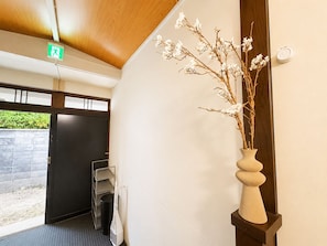 A hallway with a wooden ceiling, a white vase with branches, a trash bin, and a metal shelf unit.
