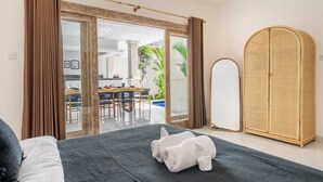 Quarto com cama, guarda-roupa, espelho e vista para uma área de jantar com mesa e cadeiras.