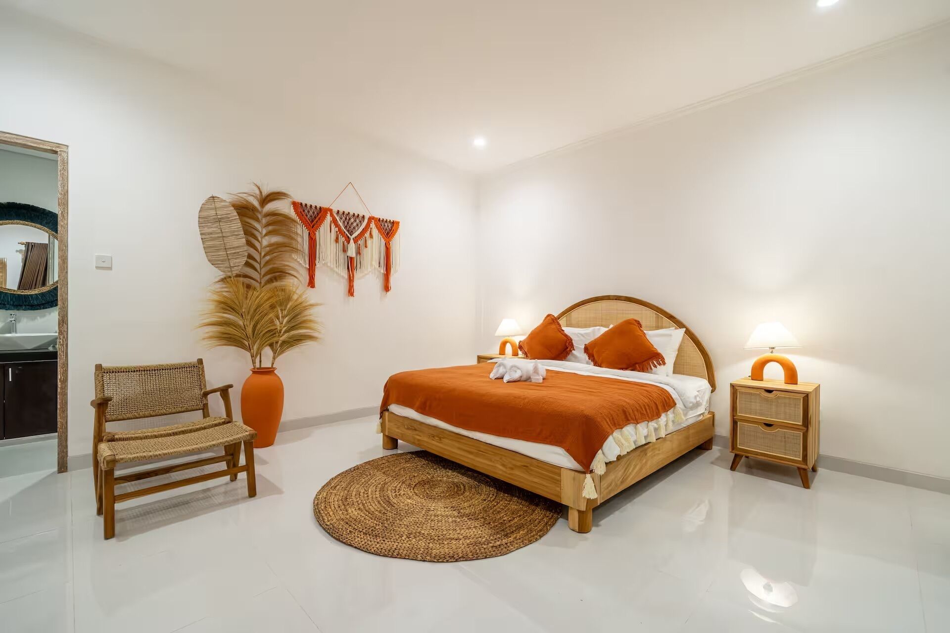 A bedroom with a bed, two bedside tables, a chair, a large potted plant, and a wall hanging.