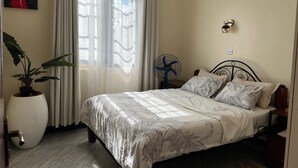 Une chambre à coucher avec un lit, une plante en pot, un ventilateur sur pied et un luminaire fixé au mur.
