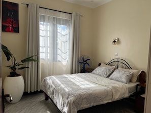 Quarto com cama, planta em vaso, ventilador e luminária na parede.