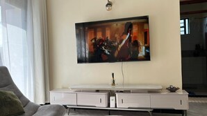 Un salon doté d’un téléviseur à écran plat fixé au mur, d’un canapé gris, d’une table basse en marbre et d’un meuble de rangement blanc avec des tiroirs.